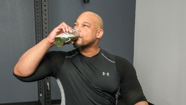 A man dressed in workout clothes drinks AG1 greens powder from a shaker bottle.